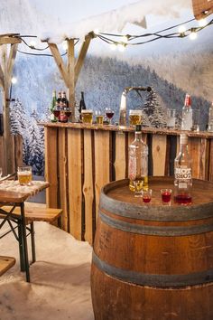 an indoor bar with several bottles and glasses on the table next to a wooden barrel