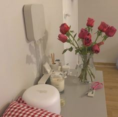 red roses in a clear vase on a table next to a mirror and other items