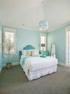 a bedroom with blue walls and green carpeted flooring, a white bed topped with lots of pillows