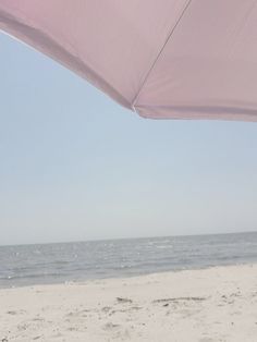 a pink umbrella on the beach with water in the backgrouund and sky in the background