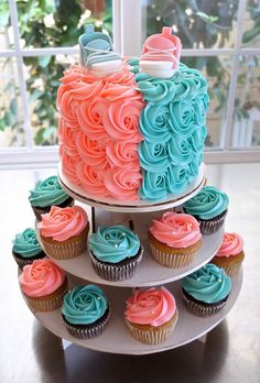 a three tiered cake with blue and pink frosting on the top, surrounded by cupcakes