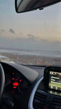 the dashboard of a car with an electronic device on it's dash board, and a city in the distance