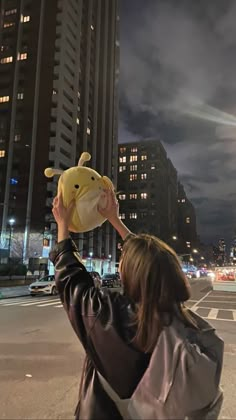 a woman holding up a stuffed animal in the air over a city street at night