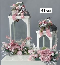 two white lanterns with pink flowers and bows on the top, one has a mirror