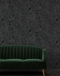 a green velvet couch in front of a black wallpapered with flowers and leaves