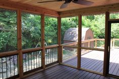 a screened porch with sliding glass doors and ceiling fan in the center, overlooking a wooded area