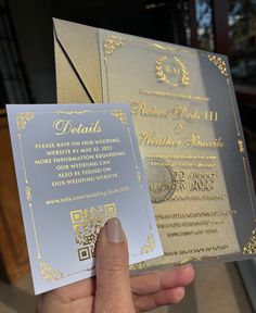 a person holding up two silver and gold wedding cards in their hand, with the same design on them