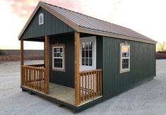 a small green house with a porch on the front and second floor, sitting in an empty lot