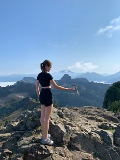 a woman standing on top of a rocky mountain holding something in her hand and looking at the mountains