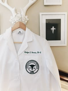 a white lab coat hanging on a wall next to framed pictures and antler's head