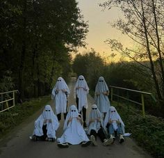 several people dressed in white sitting on the side of a road with their heads covered