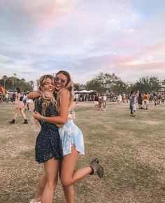 two young women hugging each other in the middle of a field at a music festival