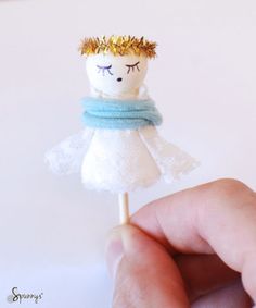 a hand holding a tiny white doll on a stick