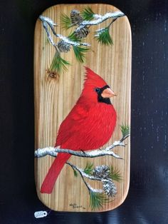 a red bird sitting on top of a wooden plaque covered in pine cones and needles