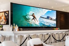 a large screen tv mounted to the side of a wall in a living room next to white chairs