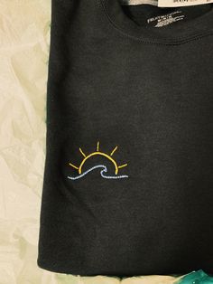 a black t - shirt with the sun embroidered on it's chest and an ocean wave