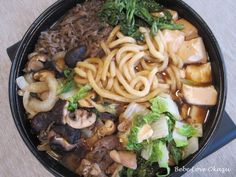 a pan filled with noodles, mushrooms and broccoli on top of a table