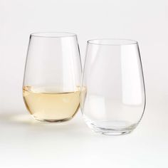 two wine glasses sitting next to each other on a white surface with one glass half full and the other half empty