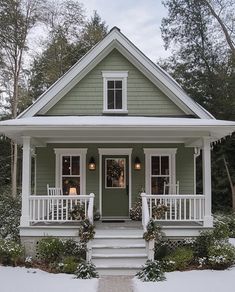 a small green house with white trim and porches covered in snow on a winter day