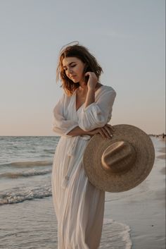 a woman in a white dress and hat on the beach