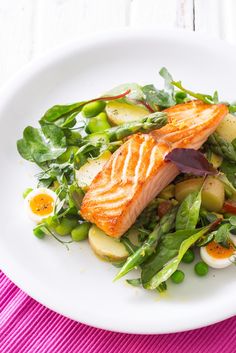 a white plate topped with salad and salmon on top of a purple table cloth next to an egg