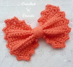 an orange crocheted bow on a white doily with the words crochet n'create written below it