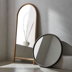 a round mirror sitting on the floor next to a white vase