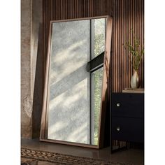 a large mirror sitting on top of a wooden floor next to a vase filled with flowers