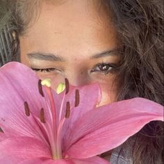 a close up of a person holding a flower in front of their face and looking at the camera