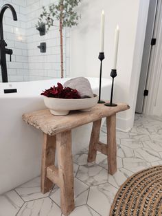 a bowl of flowers sits on a bench in front of a bathtub with candles