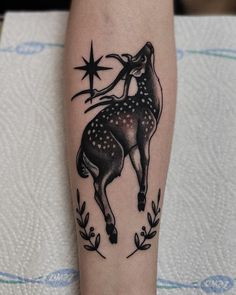 a black and white deer tattoo on the left leg, with stars above its head