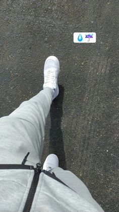 a person's feet in grey sweatpants and white sneakers, with a sticker on the ground