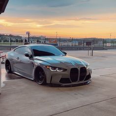 a silver sports car parked in front of a gas station with the sun setting behind it