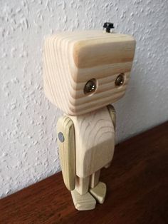 a small wooden toy with eyes and legs on a table next to a white wall