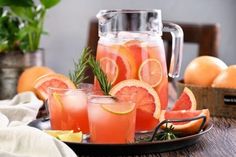 grapefruit punch with rosemary garnish in pitcher and two glasses on plate