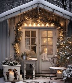 a small white house covered in snow with christmas lights and potted plants on the porch