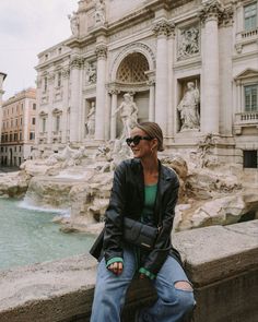 a woman sitting on the edge of a wall next to a fountain