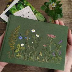 a hand holding a green book with wildflowers on it