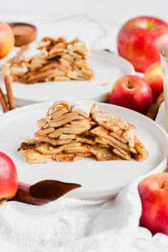 two white plates topped with slices of apple pie next to apples and cinnamon stick sticks