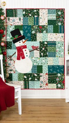 a snowman quilt hanging on the wall next to a chair and christmas tree with decorations