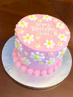 a pink and white cake with flowers on it sitting on top of a wooden table