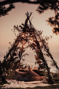 a teepee is set up with lights and pillows on the grass by the water