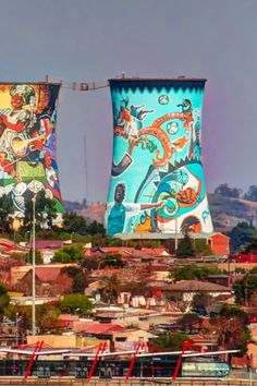 two large towers with colorful designs on them in the middle of a small town near water