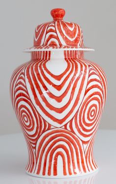 a red and white vase with swirls on it's lid sitting on a table