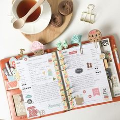 an open planner sitting on top of a table next to a cup of tea and donuts