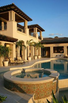 an outdoor swimming pool in the middle of a large house with palm trees and potted plants