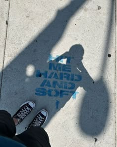 the shadow of a person standing next to a sidewalk with graffiti on it that reads me, hair and soft