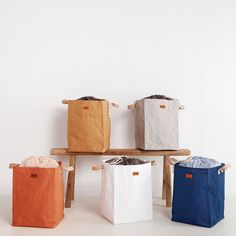 four different colored bags sitting on top of a wooden bench next to a white wall