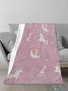 a pink blanket with white unicorns and stars on it is sitting on a couch