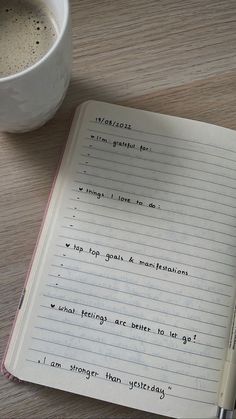 an open notebook sitting on top of a wooden table next to a cup of coffee